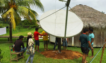 Grupo de pessoas da comunidade Yawanawá instalando uma antena parabólica para conexão à internet na aldeia.